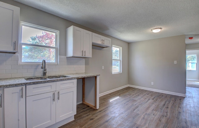 kitchen with light hardwood / wood-style flooring, sink, light stone countertops, white cabinetry, and tasteful backsplash