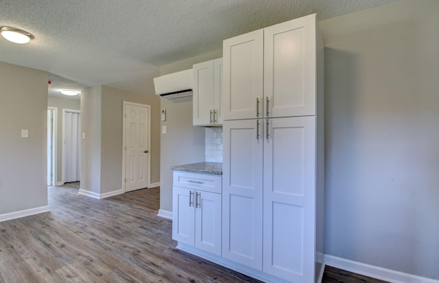 1321 S Pear St, Pine Bluff, AR 71603 - kitchen featuring a wall unit AC, white cabinetry, baseboards, wood finished floors, and a textured ceiling