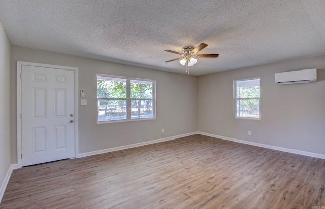 unfurnished room with ceiling fan, a textured ceiling, light hardwood / wood-style flooring, and a wall mounted air conditioner