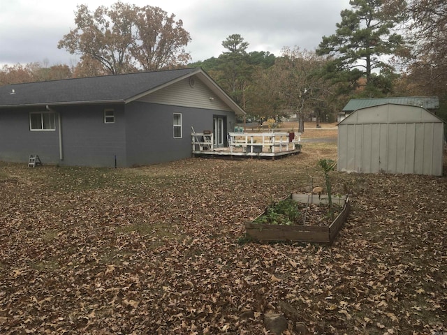 back of house with a garden, an outbuilding, a wooden deck, a storage unit, and a shingled roof