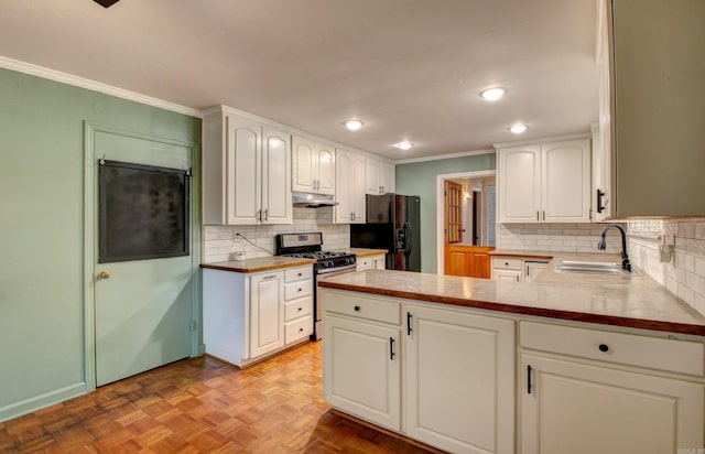 kitchen with black fridge, kitchen peninsula, stainless steel gas range, sink, and white cabinetry