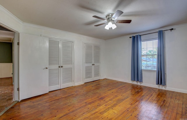 unfurnished bedroom with ceiling fan, hardwood / wood-style flooring, crown molding, and two closets