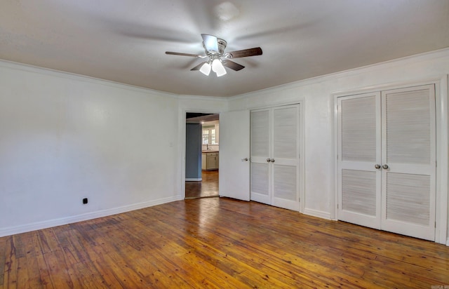 unfurnished bedroom with crown molding, dark hardwood / wood-style floors, multiple closets, and ceiling fan