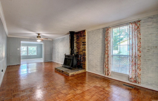 unfurnished living room with parquet floors, a wood stove, a textured ceiling, ceiling fan, and ornamental molding