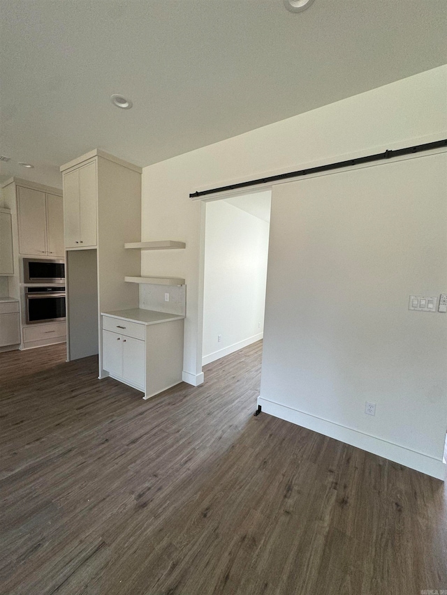 interior space with dark wood-type flooring, white cabinetry, stainless steel microwave, and a barn door