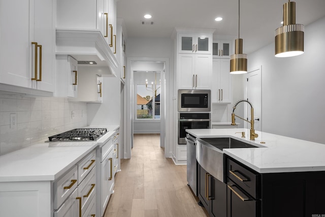 kitchen featuring a kitchen island with sink, hanging light fixtures, stainless steel appliances, white cabinetry, and light hardwood / wood-style floors