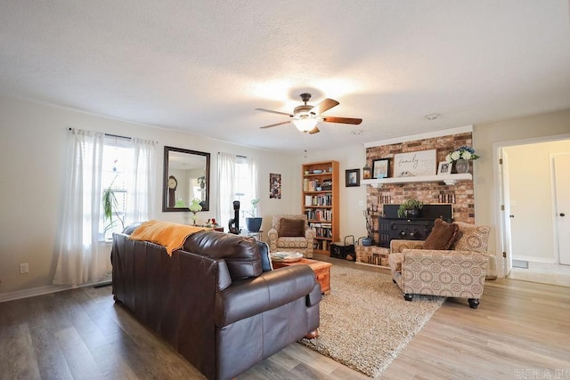 living room featuring ceiling fan, a textured ceiling, light hardwood / wood-style flooring, and a fireplace