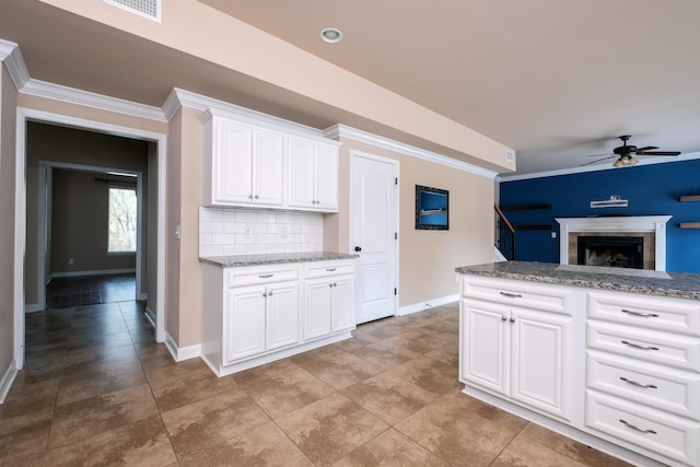 kitchen featuring tasteful backsplash, a fireplace, light stone counters, white cabinetry, and crown molding