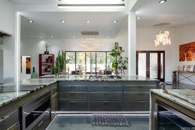 kitchen featuring a notable chandelier, stainless steel gas stovetop, light stone counters, and a healthy amount of sunlight