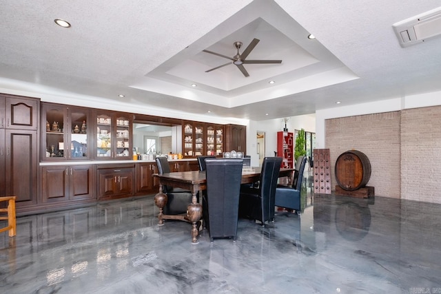 interior space with a textured ceiling, ceiling fan, and a raised ceiling