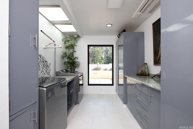 kitchen featuring gray cabinets, light stone counters, washing machine and dryer, and light tile patterned floors