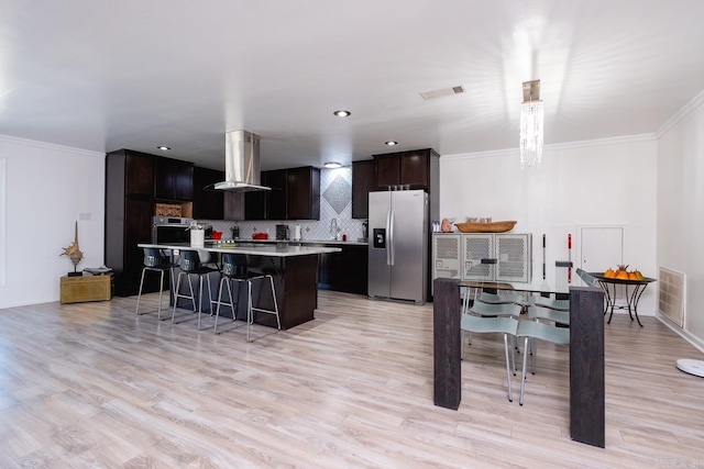 kitchen featuring dark brown cabinets, appliances with stainless steel finishes, light hardwood / wood-style floors, wall chimney exhaust hood, and a center island