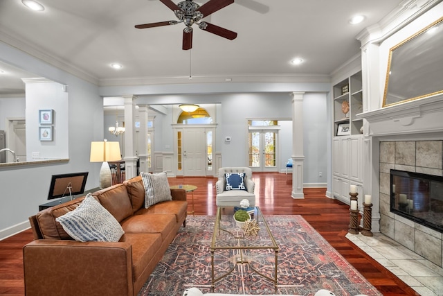 living room with crown molding, decorative columns, a tile fireplace, and dark hardwood / wood-style floors