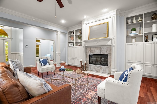 living room featuring built in features, a tiled fireplace, ceiling fan, crown molding, and dark hardwood / wood-style floors