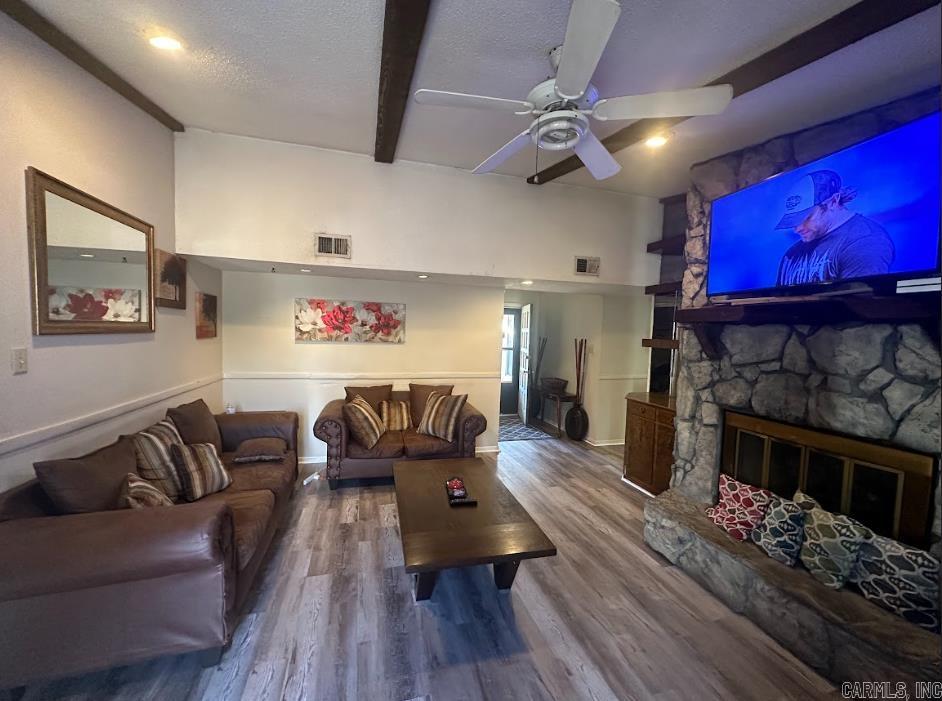 living room with beam ceiling, ceiling fan, a textured ceiling, wood-type flooring, and a fireplace