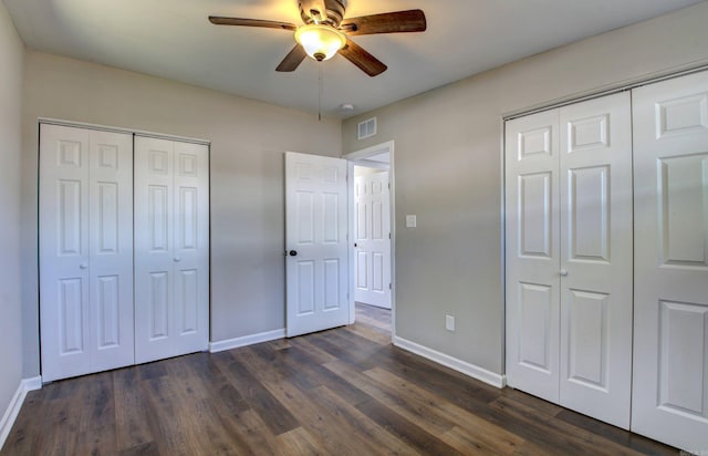 unfurnished bedroom with multiple closets, dark wood-type flooring, and ceiling fan