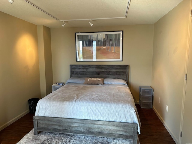 bedroom with dark hardwood / wood-style floors, track lighting, and a textured ceiling