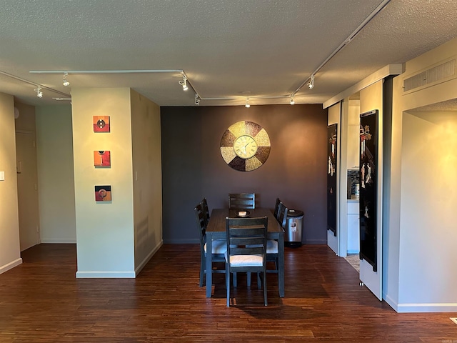 dining area with dark wood-type flooring, a textured ceiling, and track lighting