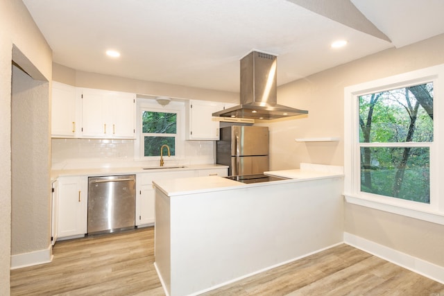 kitchen with kitchen peninsula, white cabinets, appliances with stainless steel finishes, island range hood, and light wood-type flooring