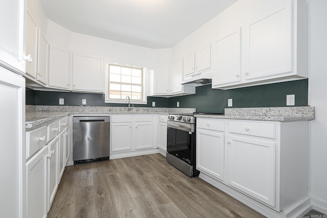 kitchen with appliances with stainless steel finishes, white cabinetry, light stone countertops, light hardwood / wood-style flooring, and sink