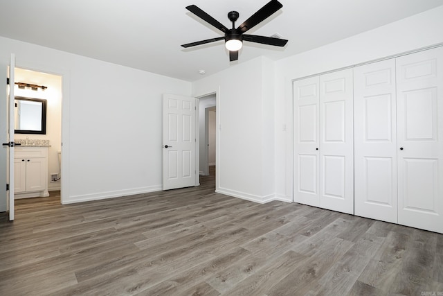 unfurnished bedroom with a closet, ensuite bathroom, light wood-type flooring, and ceiling fan