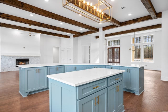 kitchen with pendant lighting, beam ceiling, a kitchen island, a stone fireplace, and blue cabinets