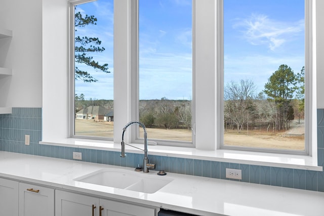 kitchen with white cabinetry, light stone counters, and sink