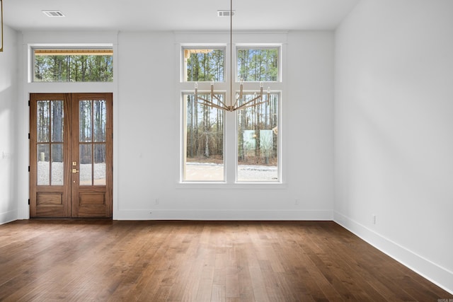 unfurnished dining area with french doors, wood-type flooring, a towering ceiling, and plenty of natural light