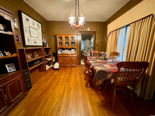 dining space featuring wooden walls, a notable chandelier, a textured ceiling, and light wood-type flooring