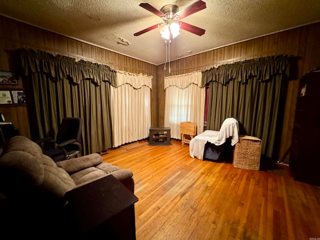 sitting room featuring wooden walls, a textured ceiling, wood-type flooring, and ceiling fan