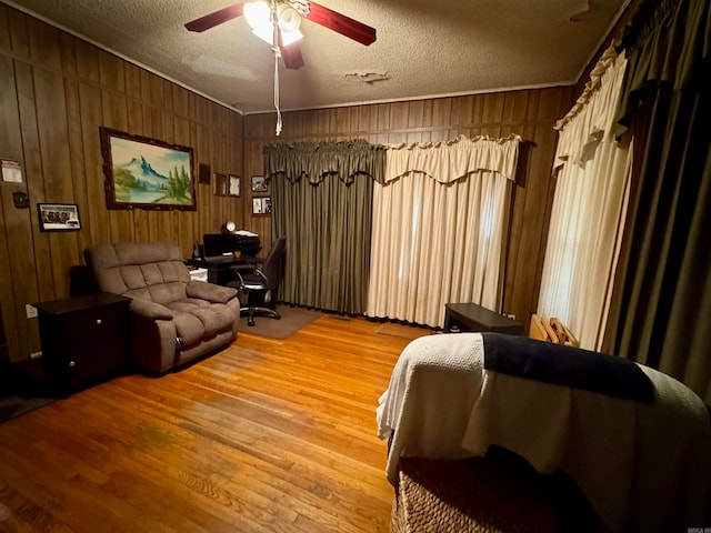 living room featuring ceiling fan, a textured ceiling, wood-type flooring, and wooden walls