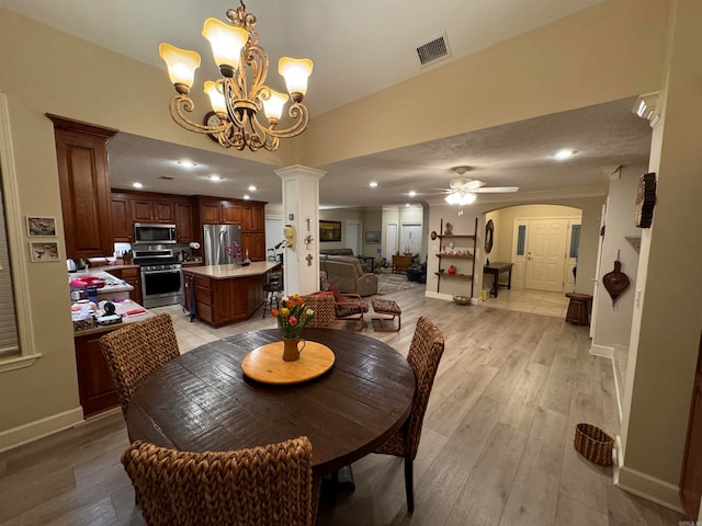 dining room with ceiling fan with notable chandelier, ornamental molding, decorative columns, and light hardwood / wood-style floors