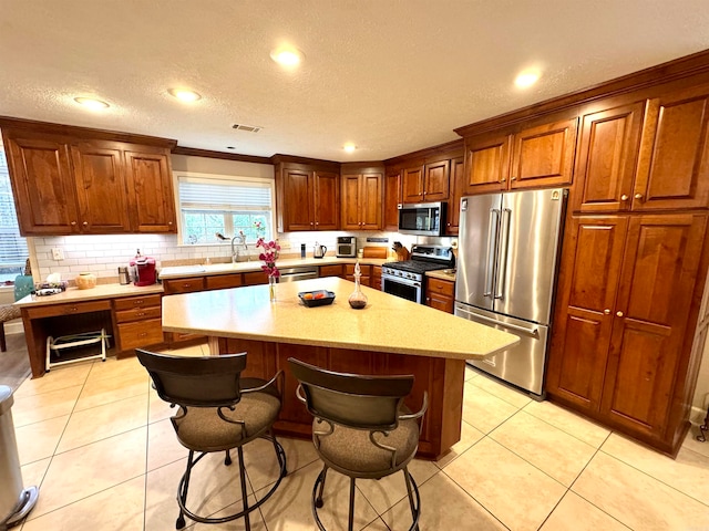 kitchen with stainless steel appliances, a kitchen bar, a center island, and light tile patterned floors