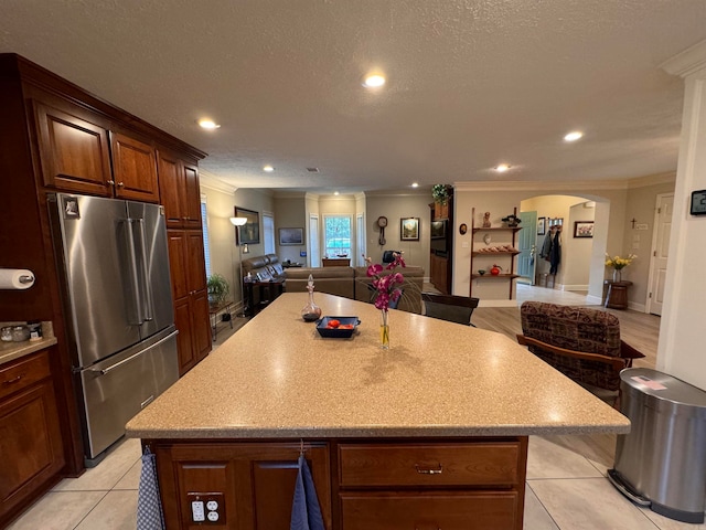 kitchen with crown molding, a kitchen island, a textured ceiling, light tile patterned flooring, and high end refrigerator