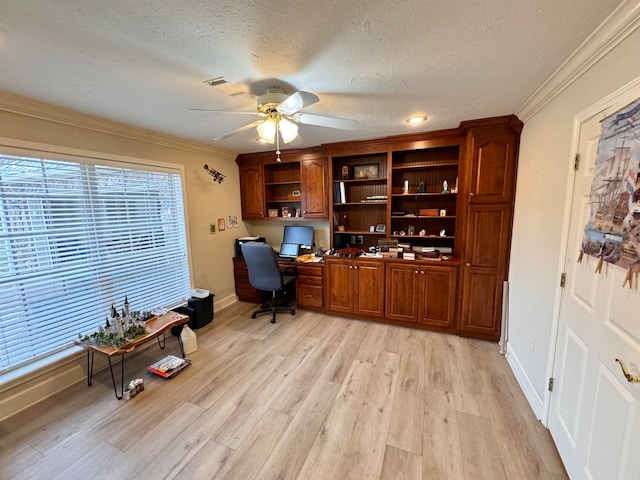 office space featuring built in desk, ornamental molding, ceiling fan, a textured ceiling, and light hardwood / wood-style flooring