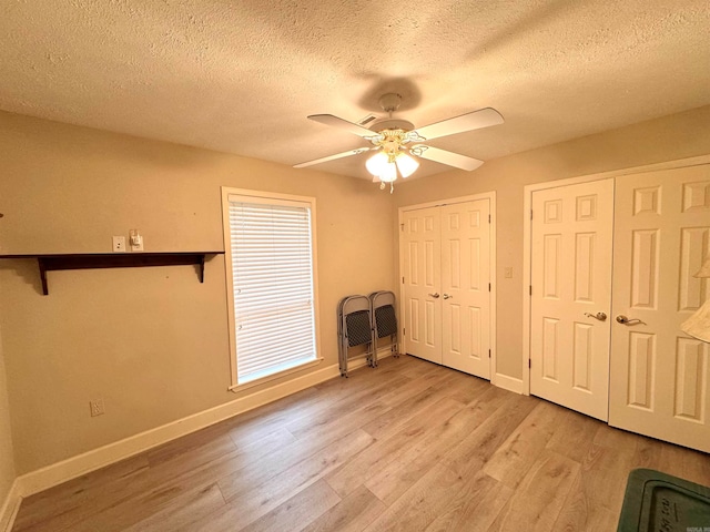 unfurnished bedroom featuring ceiling fan, two closets, a textured ceiling, and light hardwood / wood-style floors