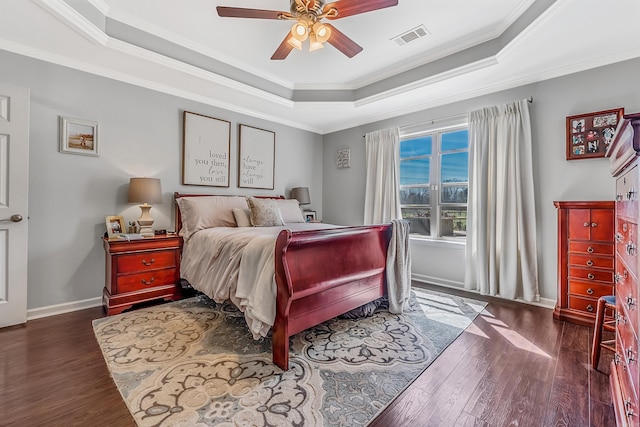 bedroom with crown molding, a tray ceiling, dark wood-type flooring, and ceiling fan