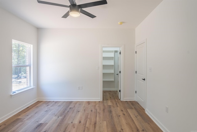 unfurnished bedroom with a walk in closet, multiple windows, light wood-type flooring, and ceiling fan