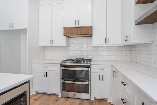 kitchen featuring backsplash, light wood-type flooring, double oven range, white cabinets, and light stone counters