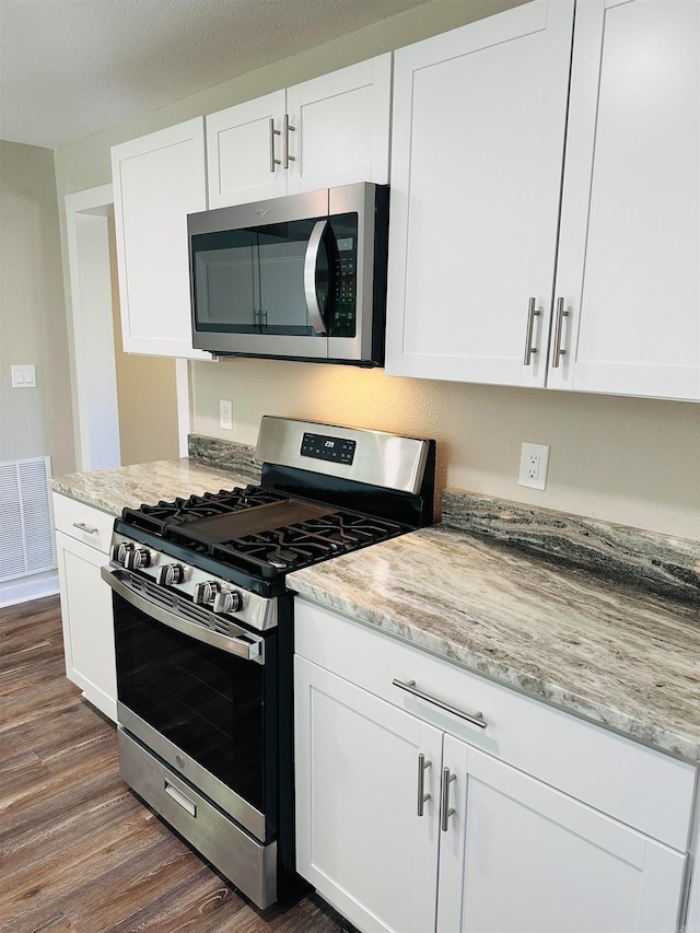 kitchen featuring appliances with stainless steel finishes, white cabinetry, light stone countertops, and dark wood-type flooring