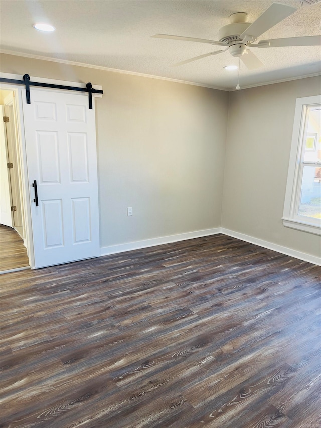 unfurnished room with crown molding, a barn door, ceiling fan, and dark hardwood / wood-style flooring