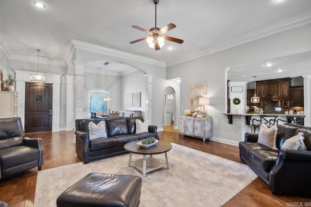 living room with ornate columns, ornamental molding, dark hardwood / wood-style flooring, and ceiling fan with notable chandelier