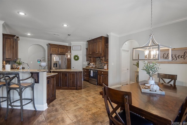 kitchen featuring a kitchen island, appliances with stainless steel finishes, an inviting chandelier, pendant lighting, and light stone counters