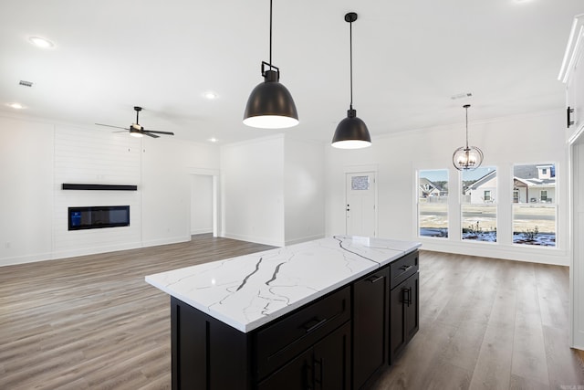 kitchen with light stone counters, pendant lighting, a fireplace, ornamental molding, and open floor plan