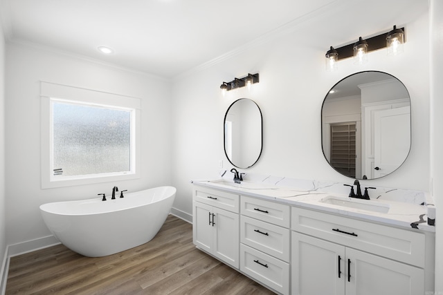 bathroom with crown molding, double vanity, a sink, wood finished floors, and a freestanding tub
