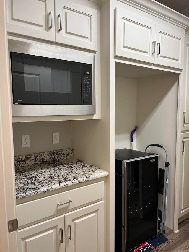 kitchen featuring white cabinetry, stainless steel microwave, wood-type flooring, and beverage cooler