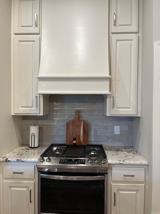 kitchen with light stone countertops, custom exhaust hood, backsplash, white cabinets, and stainless steel gas stove