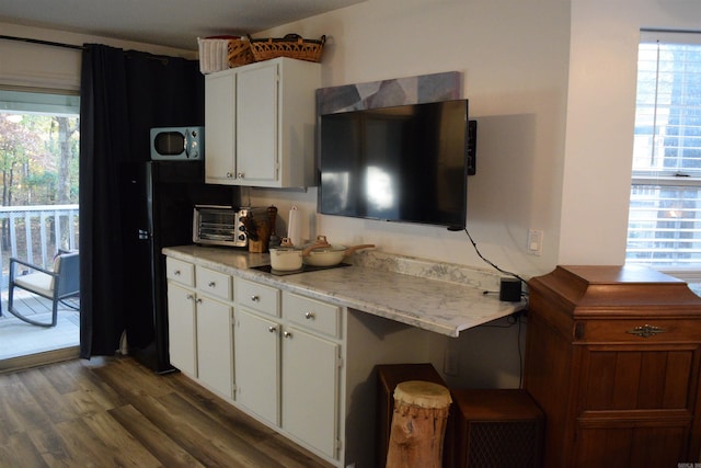 kitchen with dark wood-type flooring, light stone counters, a wealth of natural light, and white cabinets