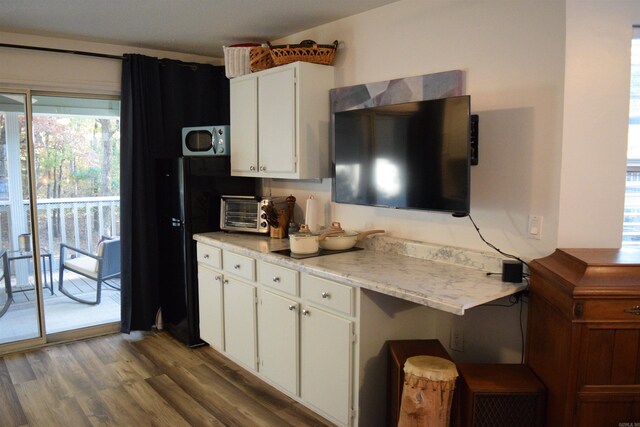 kitchen with black fridge, hardwood / wood-style floors, and white cabinets