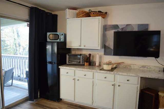 kitchen featuring light wood-type flooring, black refrigerator, and white cabinets